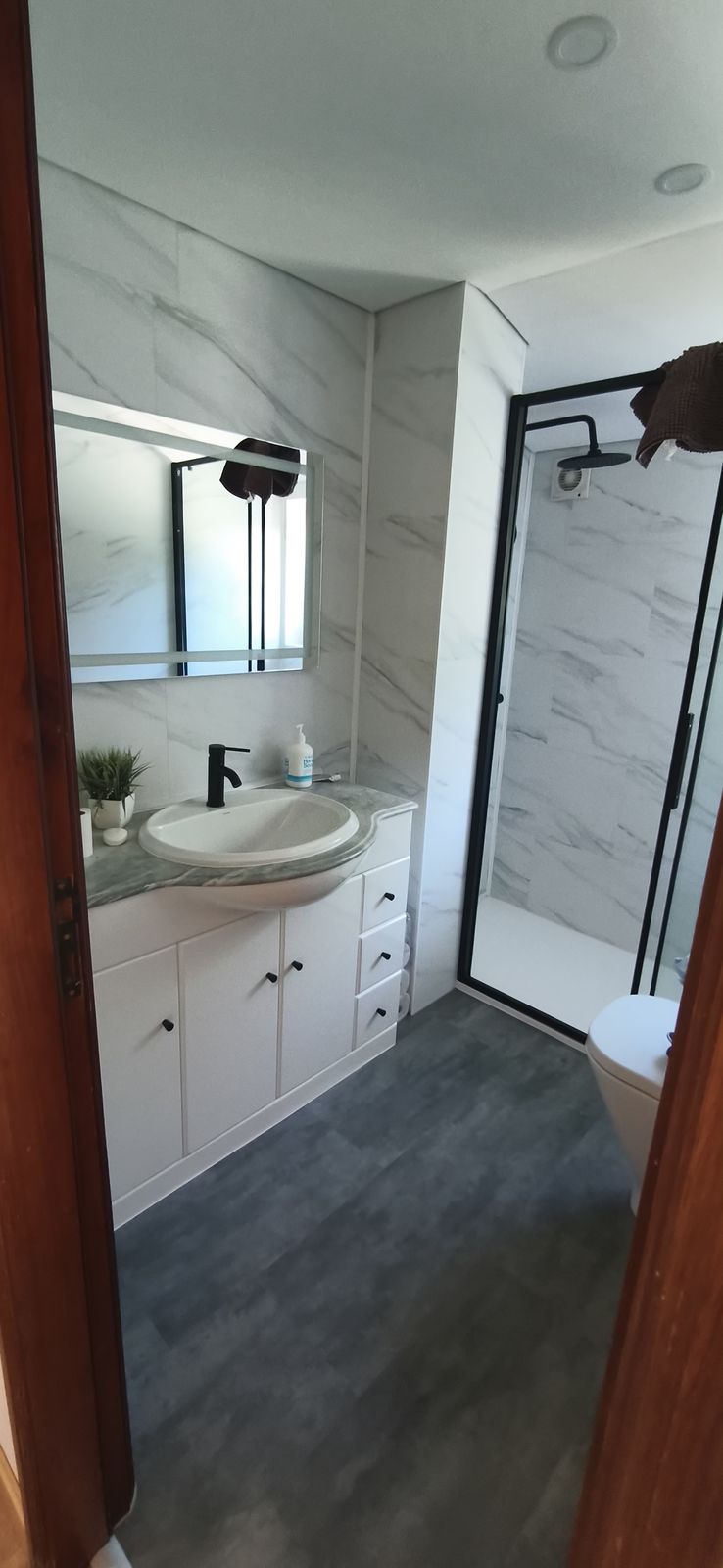 Baño renovado con ducha amplia de mampara negra y lavabo