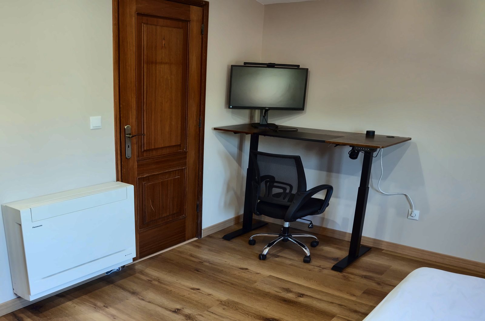 Secretária com monitor e cadeira de escritório no quarto, junto à porta de madeira