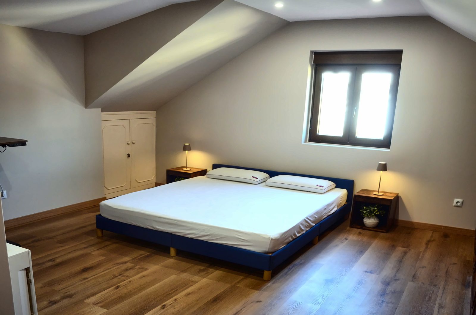 Quarto em mansarda com cama de casal, mesas de cabeceira com candeeiros e janela
