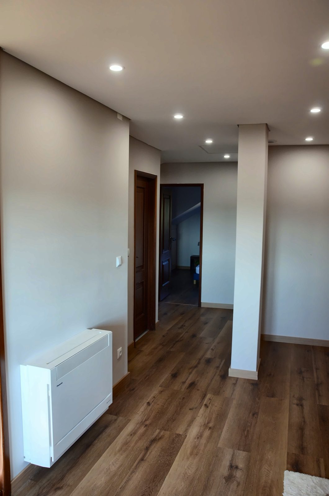 Corredor luminoso com chão de madeira e focos embutidos