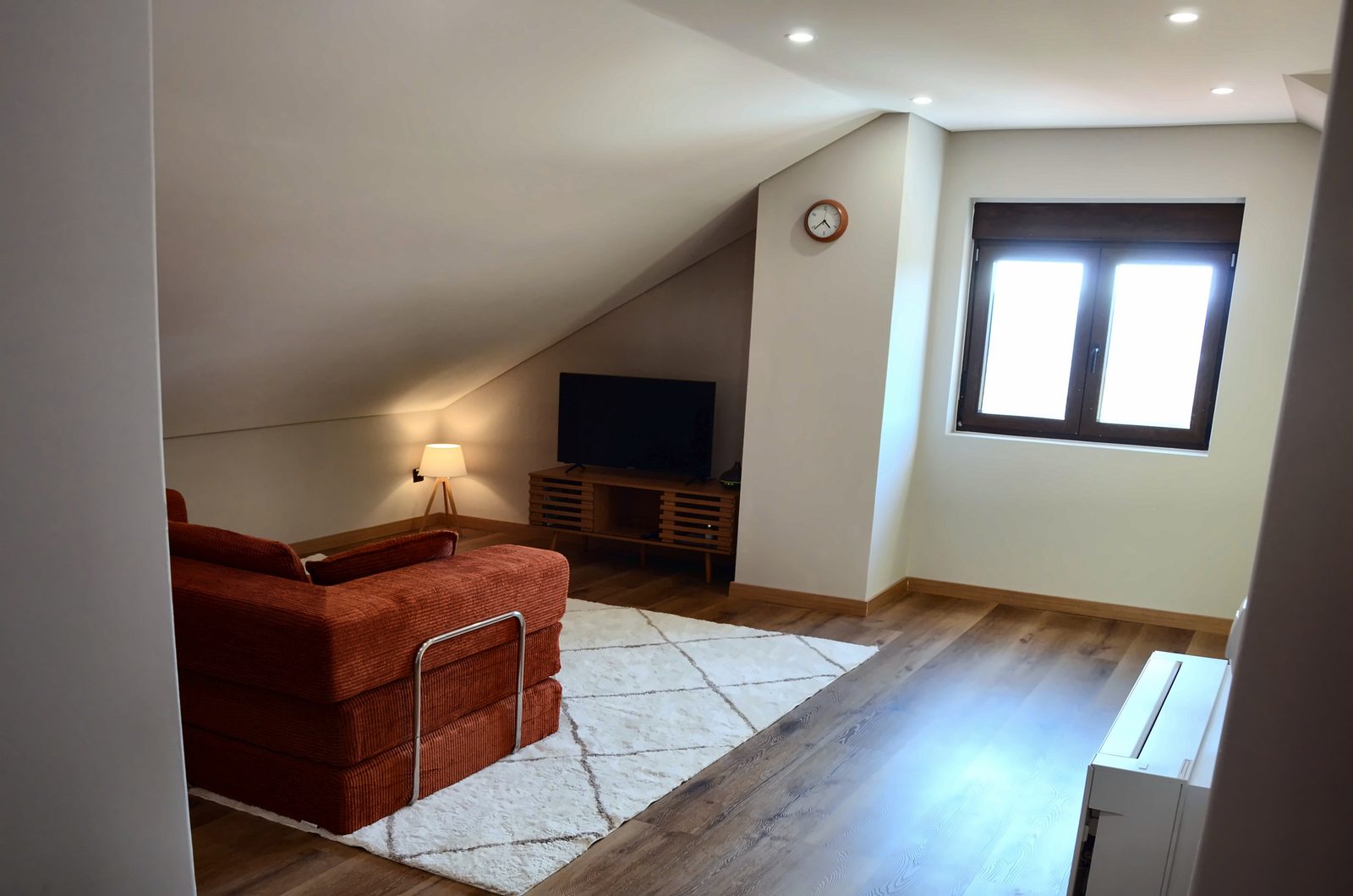 Canto da sala com sofá, televisão, candeeiro e janela
