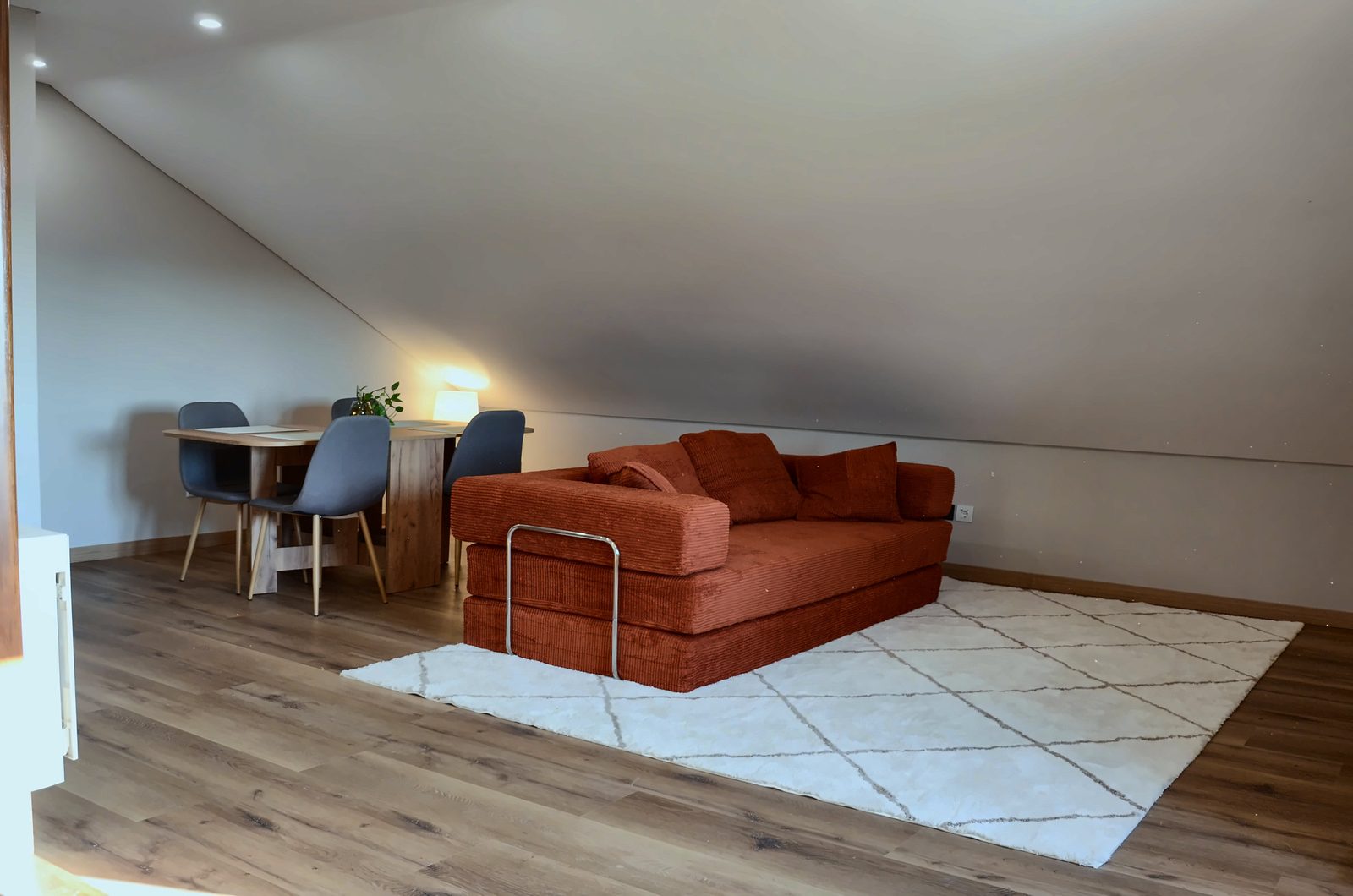 Sala com sofá cor de terracota sobre tapete claro, mesa de jantar e chão de madeira