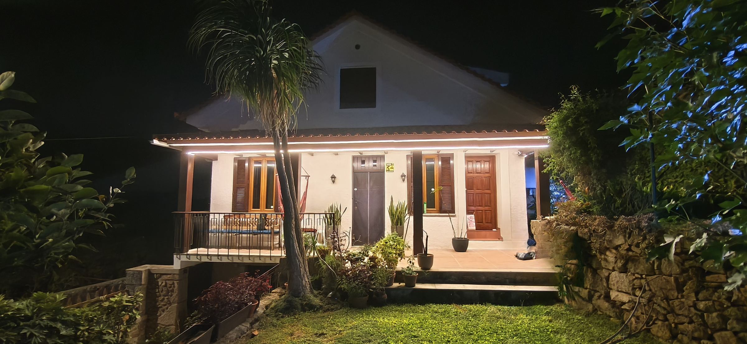 Fachada de la casa de piedra de 1937 iluminada de noche, vista desde el jardín