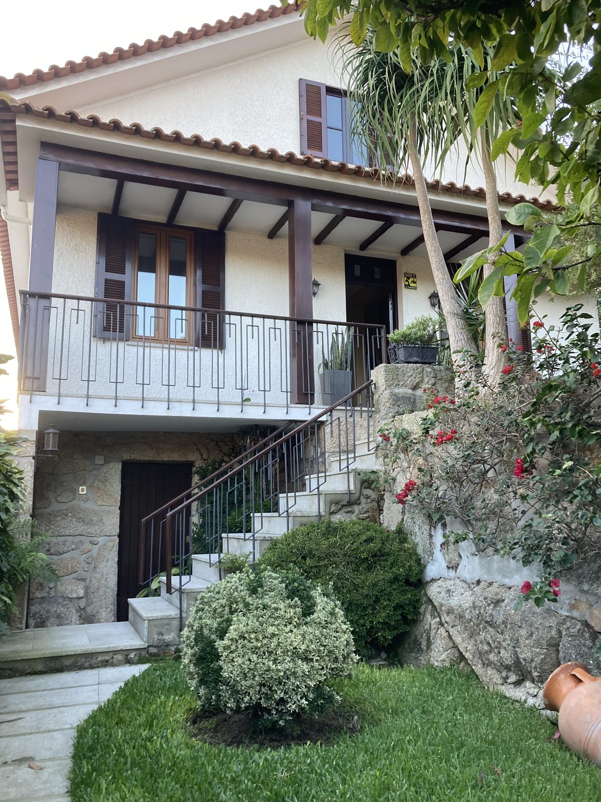 Fachada da casa com escada exterior, varanda e jardim com arbustos